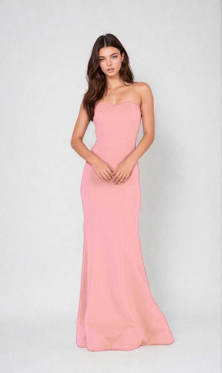 A woman poses against a plain backdrop wearing the Strapless Sweetheart Long Prom Dress: Chicas C011, a light pink, floor-length gown with a fitted bodice—an elegant and affordable choice for formal occasions.